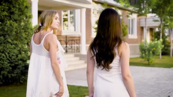 Vista trasera de dos chicas elegantes caminando por la calle y charlando en verano . — Vídeo de stock