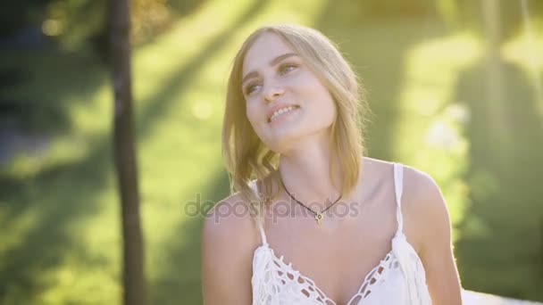 Очаровательная молодая блондинка позирует под летним солнцем и смотрит в сторону — стоковое видео
