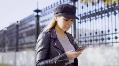 Genç ve çekici bir kadın sokakta yürüyor ve smartphone üzerinde bir ileti yazdırır, hanım bir telefon elinde tutuyor