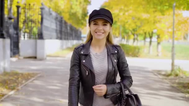Μια νεαρή και όμορφη γυναίκα βόλτες κάτω από την οδό με ένα χαμόγελο στο πρόσωπό της, μια κυρία που μοιάζει με μια χαρούμενη περαστικό — Αρχείο Βίντεο