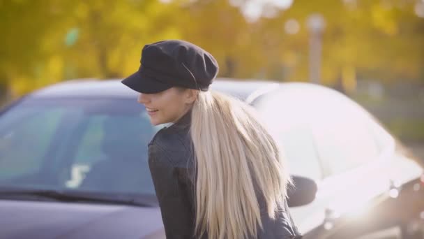 Eine süße und fröhliche Frau mit Mütze auf dem Kopf lacht und lächelt, die Dame steht neben dem Auto, in der Hand die Schlüssel — Stockvideo