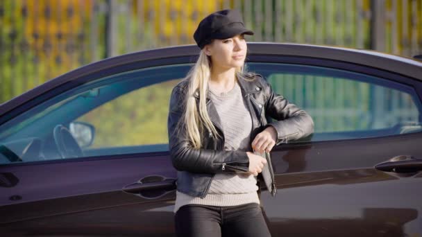 Una mujer atractiva se para cerca de su coche y endereza su cabello, tal vez una dama está esperando a alguien en un día de otoño — Vídeos de Stock