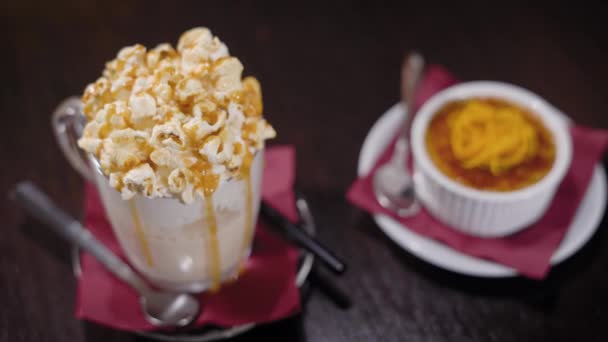 Un tiro cercano a un batido con espuma cremosa y sabor caramelo o vainilla, en el platillo es un tubo, junto al postre dulce — Vídeos de Stock