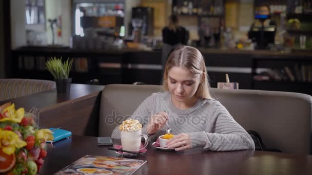 Eine junge und hübsche Frau isst Dessert und trinkt Milchkrapfen mit Karamellgeschmack, eine Dame liebt es, sich in einem Café mit köstlichen Gerichten zu beschäftigen — Stockvideo