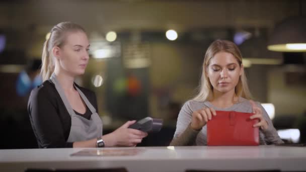 Een jonge en mooie vrouw neemt een bankkaart van haar handtas om te betalen van de rekening in het restaurant door de betaling terminal — Stockvideo