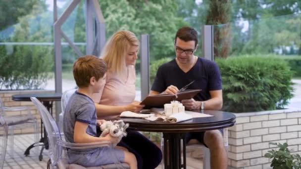 Family on restaurant terrace sitting and choosing dishes from menu together — Stock Video