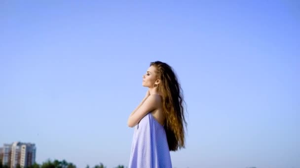 Vista lateral de la sensual mujer con el pelo largo posando en el cielo azul manteniendo los ojos cerrados . — Vídeos de Stock