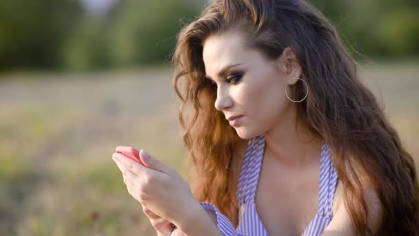 Jovem morena elegante usando smartphone enquanto posando no fundo do campo de país . — Vídeo de Stock