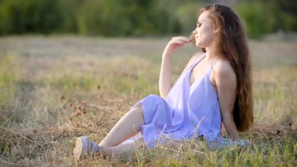 Unga trendiga brunett i ljusa sommarklänning som sitter på gräset i fältet poserar med slutna ögon. — Stockvideo