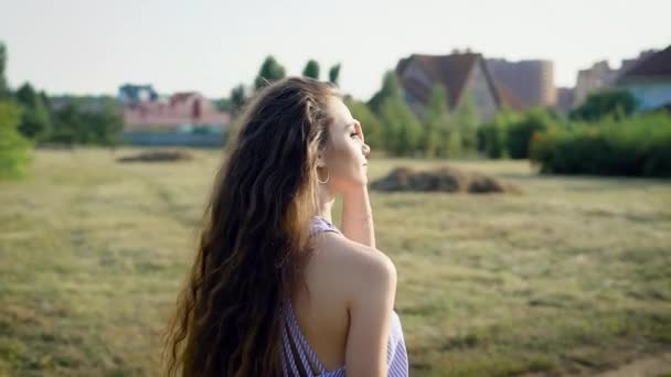 Обратный вид женщины с длинными волосами, позирующей на фоне сельской местности, смотрящей в сторону солнечного света . — стоковое видео