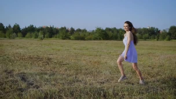 Vista lateral de chica en vestido en movimiento de correr sobre hierba de campo en paisaje urbano . — Vídeos de Stock