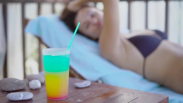 Žena, která leží v houpací síti a je oblečen v plavkách se táhne ruku do sklenice s nápojem, dáma se opírá o dovolené — Stock video