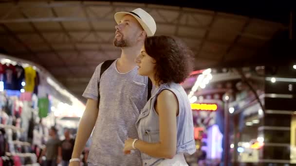 Un hombre y una mujer felices están caminando en el mercado nocturno. Una pareja de vacaciones fue de compras, eligen recuerdos y cosas. Bazar. — Vídeos de Stock