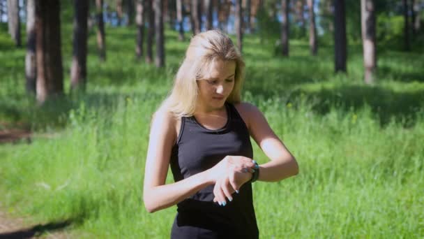 En ung blond kvinna ändrar inställningar på en smart klocka, en idrottsman som driver körningar vill veta hur många kilometer sprang hon — Stockvideo