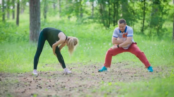 Friends do an exercise to stretch the muscles of the legs and back in the park, they rest their hands on each other and press on the back — Stock Video