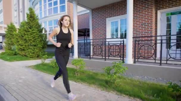 Deportiva corriendo a la luz del sol por la acera de la calle en verano — Vídeo de stock