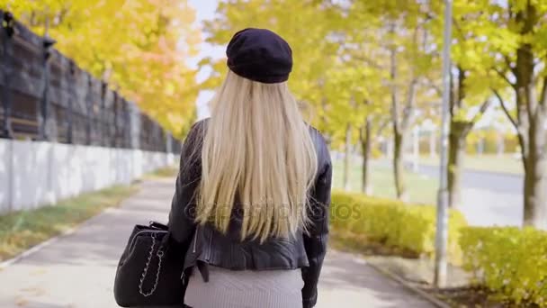 Щаслива молода жінка йде через алею в міському парку восени і звертається до камери і стикається з рукою — стокове відео