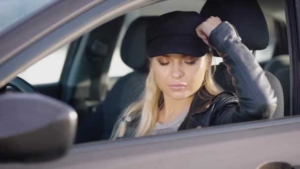 Περίλυπος χαριτωμένο γυναίκα με μακριά ξανθά μαλλιά κάθεται μέσα σε ένα αυτοκίνητο σε ένα κάθισμα οδηγού, περιμένοντας για κάποιον — Αρχείο Βίντεο