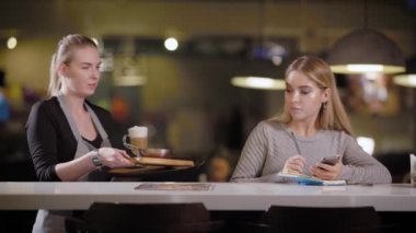 Öğrenci kız kafede oturan ve yazma kağıt, defterinde Garson kahve ve yemek getiren smartphone, bilgi için arıyorsunuz