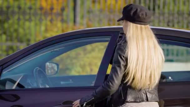 Genç sümük sarışın karanlık otomobil, açık kapı, direksiyon başında oturan ve bir araba güneşli sonbahar günü başlayan yaklaşıyor — Stok video