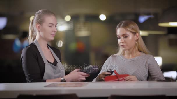 Официантка приближается к женщине-посетителю ресторана с платежным терминалом для оплаты счета — стоковое видео