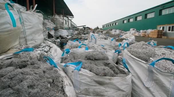 Basura de metal triturado está embalando en grandes bolsas de plástico blanco, acostado en un suelo al aire libre en un patio de demolición en el día — Vídeo de stock