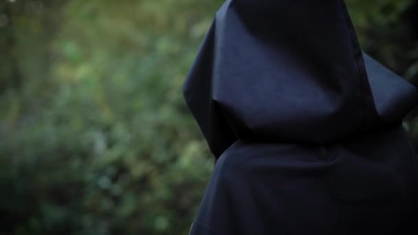 Vrouw draagt zwarte regenjas met kap loopt snel in een dichte enge bos in saai weer in avond — Stockvideo