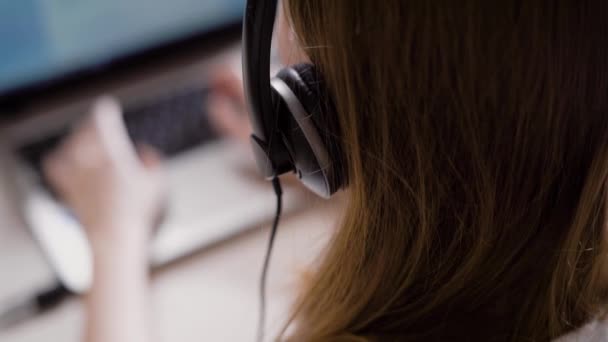 Обрізати жінку, що працює офісним помічником, використовуючи ноутбук та навушники — стокове відео