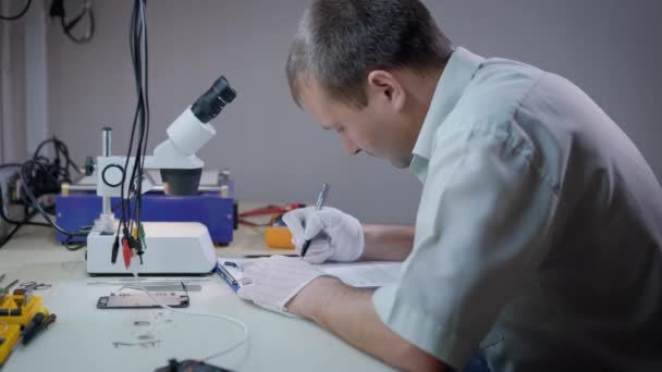 Científico serio escribiendo informe mientras trabaja en un nuevo laboratorio especial — Vídeos de Stock