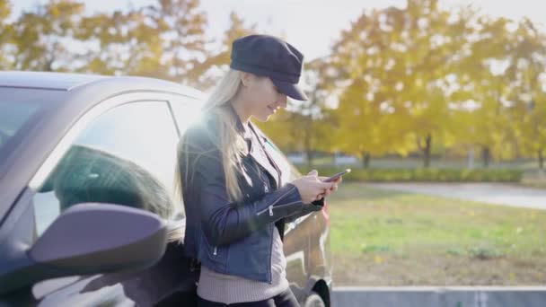 Ελκυστικό νεαρό μοντέλο με smartphone θέτοντας κοντά σε αυτοκίνητο στην πτώση πάρκο — Αρχείο Βίντεο