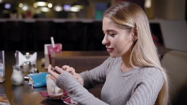 Жінка має каву в кафе і дивиться телефон за столом — стокове відео