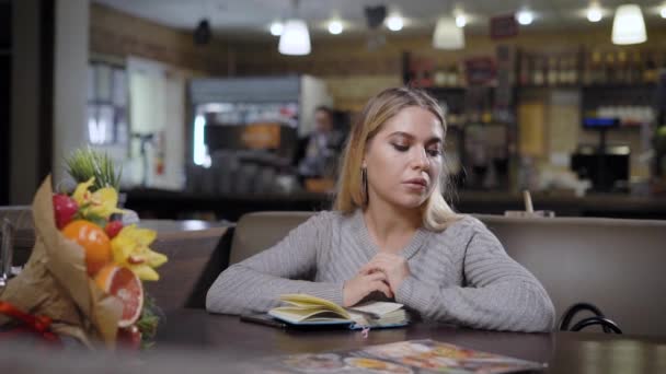 Charmante peinzende model poseren met Kladblok aan tafel in de moderne cafetaria — Stockvideo