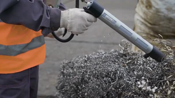 Промышленный рабочий использует прибор для сканирования кучи серебряных спиралей металлических стружек — стоковое видео