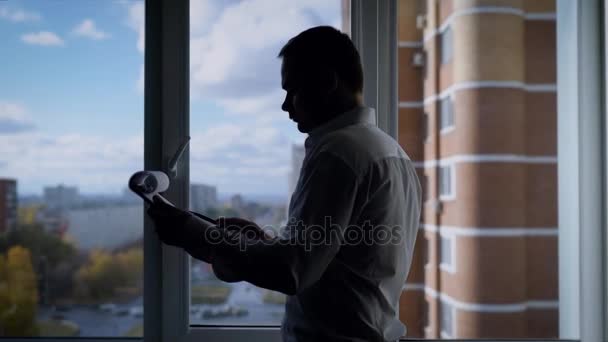 Hombre de negocios concentrado está leyendo un contrato en hojas de papel, de pie frente a la ventana en su oficina en el día de otoño — Vídeo de stock