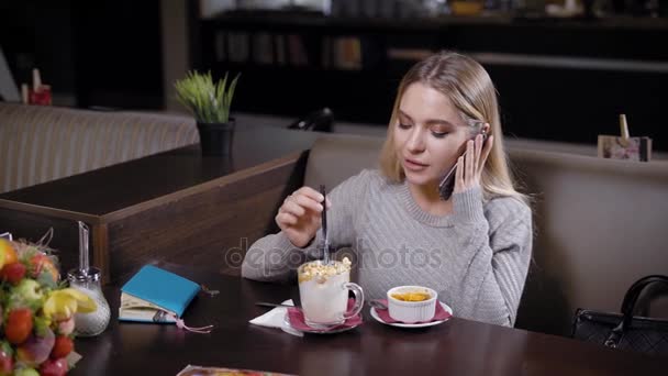 Mulher bonita fala em um telefone em um café . — Vídeo de Stock