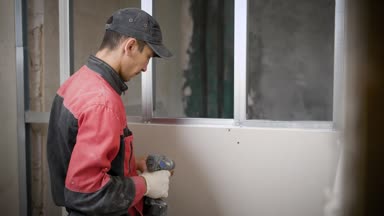 tamirci bir alçı panosu profilleri, kendi kendine vurma vida ve elektrikli tornavida kullanarak tamir ediyor