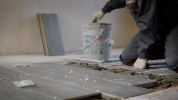 Carrelage applique un mélange de construction sur un plancher pour le montage de carreaux de céramique, maître est debout sur un genoux sur un plancher — Video