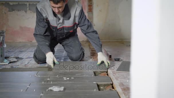 Zkušený pracovník dělá Obkladačské práce, leží šedé dlaždice na podlaze v místnosti úřadu s oknem — Stock video