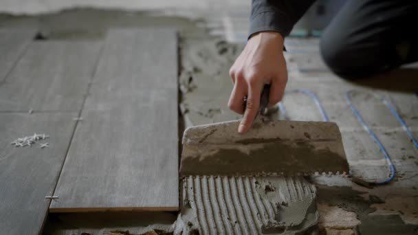 La mano di padroni tiene la spatola con denti e equalizza la malta da costruzione su un pavimento durante il processo di installazione di piastrelle — Video Stock