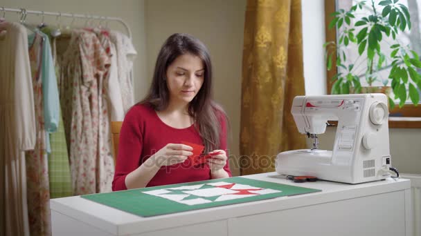 Взрослая женщина делает аппликацию из кусочков ткани, лежа на столе в дневное время в мастерской — стоковое видео