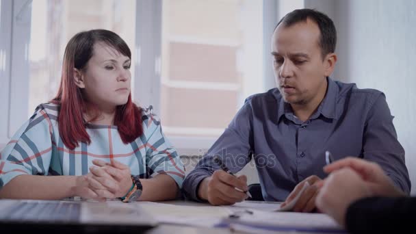 Jonge echtgenoten luisteren naar wat de advocaat zegt aan hen, de man met Ernst schrijft informatie op een stuk papier, kwamen mensen voor advies — Stockvideo