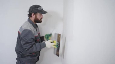 Yetişkin bir Oluşturucu sakalı ile duvar uzun spatula ve alçı ile hizalar, adam kompozisyon yüzeye uygulanır.