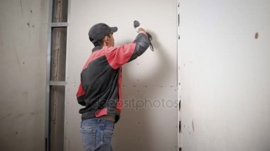 Bir profesyonel Oluşturucusu vida çivi alçı, adam yapılmış duvar içine bir tatbikat elinde tutar ve çivi takunya