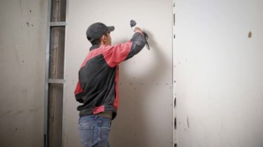 Bir profesyonel Oluşturucusu vida çivi alçı, adam yapılmış duvar içine bir tatbikat elinde tutar ve çivi takunya