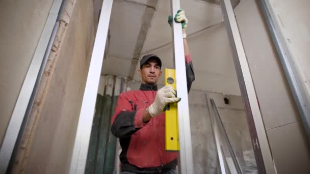 Un constructor profesional monta el marco de la pared durante la reparación de la habitación, utilizando el nivel mide el grado de inclinación — Vídeos de Stock