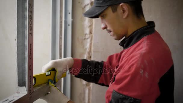 Een jonge werknemer die werkt op een site voor bouwwerkzaamheden met aluminium profielen, hulpprogramma's voor het meten van het niveau, de man levert reparaties in het appartement — Stockvideo