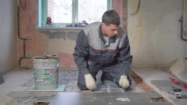 Работник в форме здания проверяет уровень поверхности на керамико-гранитной плитке во время укладки пола в строящейся квартире — стоковое видео