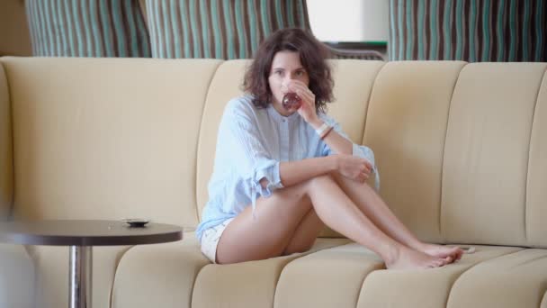 Вміст молода жінка охолоджує на дивані і п'є освіжаючий чай — стокове відео