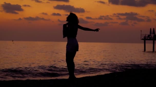 Silhouette of happy slim woman is jumping on a sea coast in evening time after sunset and rising hands — Stock Video