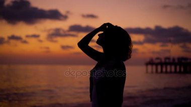 kadın silüeti alacakaranlık günbatımı gökyüzü, deniz, dua ve eller yükselen elleri katlanır isteyen bir arka plan üzerinde bir deniz kıyısında duruyor